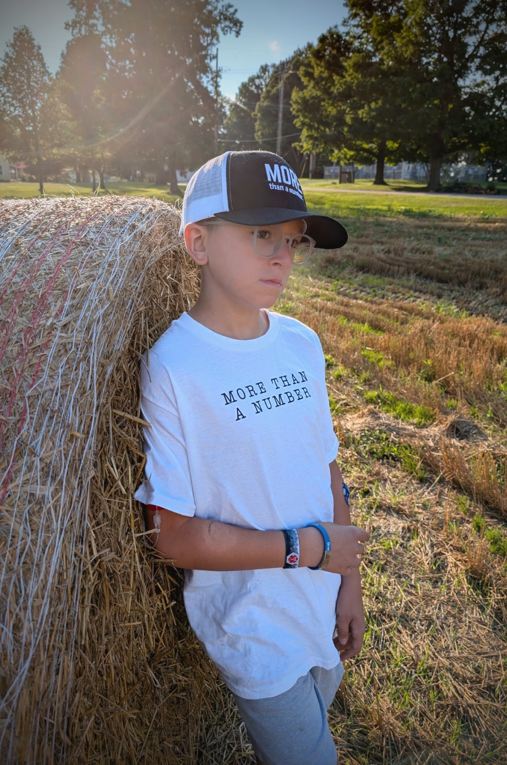 Elias wearing the More Than a Number shirt and hat beside a hay bale